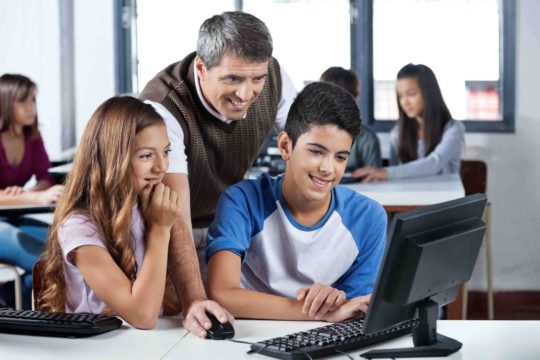 Male teacher helping two students at a computer